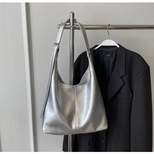Détail d'un grand sac cabas argenté avec texture plissée et bandoulière sur un cintre