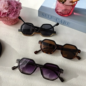 Three polygon sunglasses in black gold, tortoise shell and gradient grey on a white table