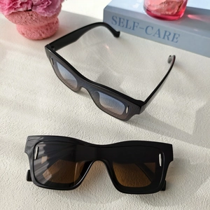 Vue à plat de lunettes de soleil carrées noires avec rivets argentés sur fond blanc