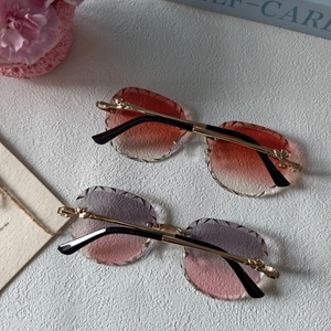 Rimless oval sunglasses with gradient lenses and diamond-cut edges on a textured surface