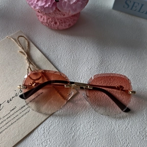 Close-up of rimless oval sunglasses with diamond-cut pink gradient lenses and gold temples