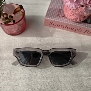 Détail de lunettes de soleil rectangulaires gris-violet sur fond cadeau rose