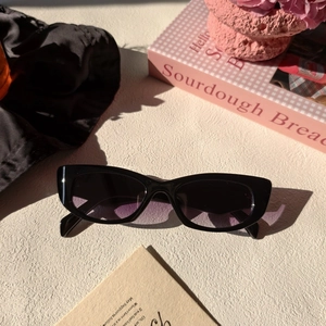 Détail de lunettes de soleil œil-de-chat noires avec verres dégradés violets