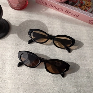 Flat lay of two black oval cat-eye sunglasses with dark lenses on a stylish pink setting