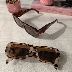 Detail of square oversized tortoiseshell sunglasses on a white textured marble surface