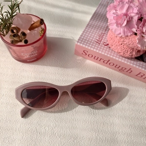Detail of pink cat-eye sunglasses with gradient lenses on a textured white surface