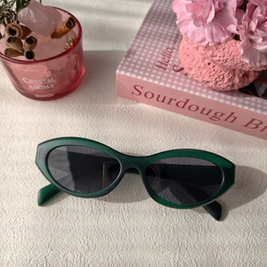 Dark green cat-eye sunglasses with matte resin frames and dark lenses on a pink desk