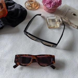 Retro narrow rectangular sunglasses in black and tortoiseshell displayed on a stone surface
