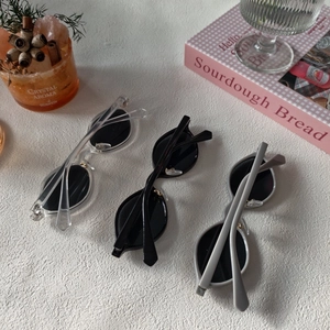 Three pairs of vintage oval sunglasses in clear, black and grey resin frames on white texture