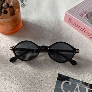 Detail of retro oval black sunglasses featuring metal stripe accents on a textured surface
