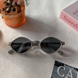 Close-up of grey oval retro sunglasses with gold metal accents on textured surface