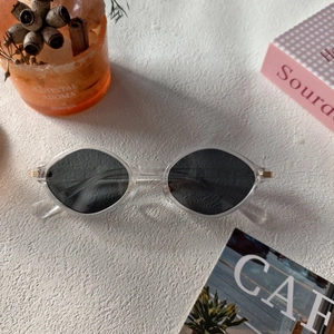 Detail of oval resin sunglasses with transparent white frames and gold metal hinge accents