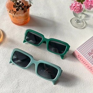 Vue à plat de lunettes de soleil carrées en résine vert foncé et menthe sur fond blanc