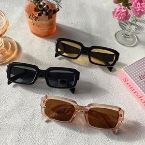 Détail de trois lunettes de soleil rectangulaires rétro noires et rose thé sur table