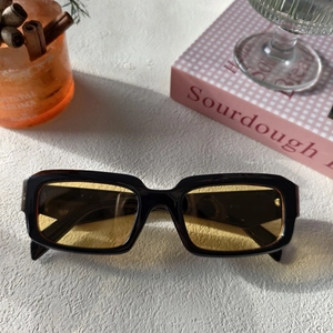 Gros plan de lunettes rectangulaires noires aux verres ambrés à côté d'un livre et d'un café