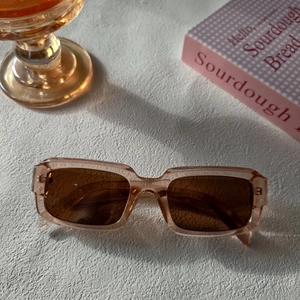 Détail de lunettes de soleil carrées champagne translucide avec verres bruns sur fond blanc