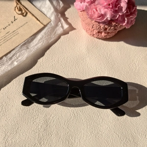 Macro detail of retro black slim-frame sunglasses with dark lenses on a textured surface