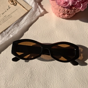 Close-up of retro cat-eye sunglasses with black frame and brown lenses on a floral background