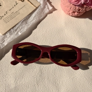 Detail of retro red square sunglasses with brown lenses on a textured cream background