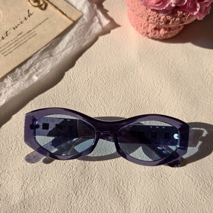 Stylish translucent purple cat-eye sunglasses with blue lenses on a stone surface