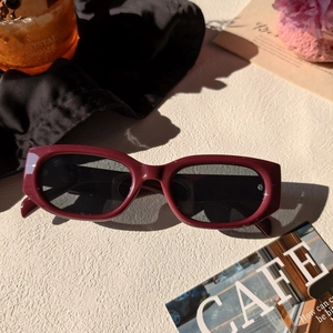 Détail de lunettes de soleil ovales bordeaux avec verres foncés et rivet en métal