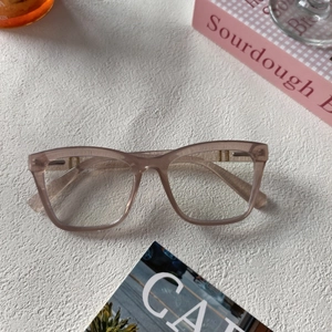Détail de la monture en résine rose thé semi-transparente sur une surface minimaliste