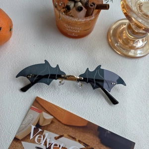 Close-up of frameless bat-wing sunglasses with grey lenses and golden metal bridge on table