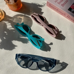 Close-up of cat-eye sunglasses with golden metal hinges in pink, green and blue