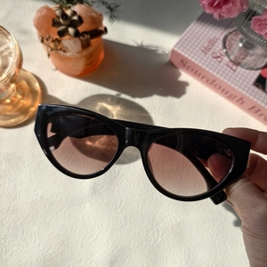 Close-up of black cat eye sunglasses with gradient lenses held over an aesthetic desk