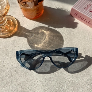 Cat eye sunglasses with blue-gray frames on a minimalist textured surface with lifestyle props