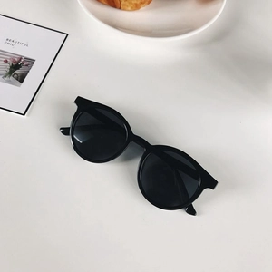 Dettaglio degli occhiali da sole neri rotondi su scrivania bianca con carte decorative