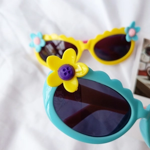 Nahaufnahme der Kinder-Sonnenbrille mit Blumenmuster und Wellenrand in Gelb und Blau