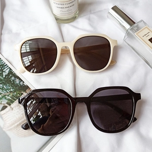 Retro oversized sunglasses in cream and black frames on a textured fabric background