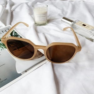 Beige oversized polygonal sunglasses on white fabric with perfume and candle props