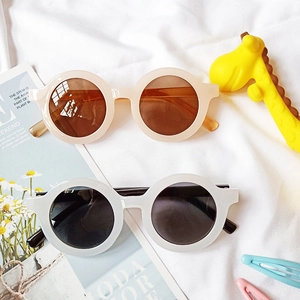 Détails de lunettes de soleil rondes pour enfants en beige et blanc sur fond de tissu chic