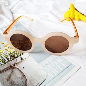 Détail de lunettes de soleil rondes pour enfants avec cadre beige et branches orange chaud