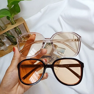 Detail view of pink and black oversized square sunglasses frames held by a model