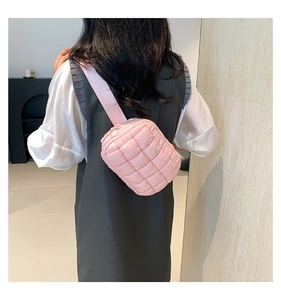 Pink quilted cloud crossbody bag with wide shoulder strap worn by a model in soft lighting
