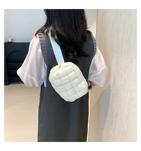 Close-up of beige quilted crossbody bag featuring adjustable webbing strap on a model