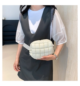 Detail of cream quilted waist bag with puffer texture and grid pattern on a female model