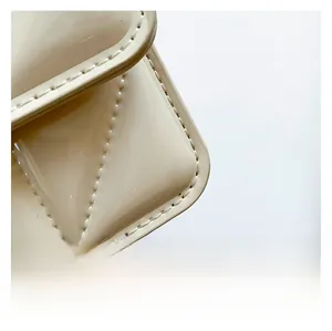 Gros plan des coutures à carreaux sur le sac à main en cuir verni de couleur crème