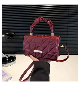 Détail du sac en cuir verni bordeaux brillant avec motif matelassé et poignée plissée