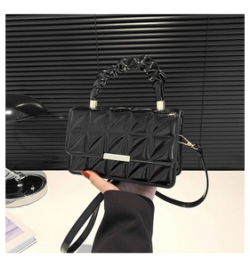 Détail d'un sac à main noir en cuir verni brillant avec motif matelassé et boucle dorée