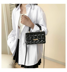Détail du sac bandoulière en cuir verni noir avec motif matelassé et boucles dorées