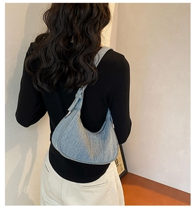 Model wearing light blue denim half-moon underarm bag with silver metal buckle detail