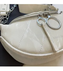 Detail of cream beige crescent bag showing glossy texture and silver chain strap