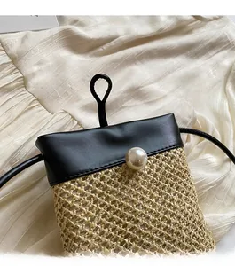 Detail of straw crossbody bag with faux pearl closure and black leather trim