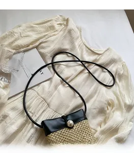 Detail of woven straw mini bag featuring a black leather flap and pearl buckle closure