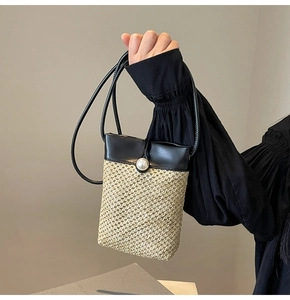 Detail of hand-woven straw phone bag featuring a black leather flap and large pearl closure