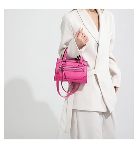 Détail du sac bandoulière en cuir rose vif avec pompon et fermeture éclair sur blazer